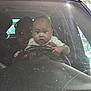 baby, infant, child, steering_wheel, car, windshield, dirty_windshield, garage, surprised_expression, adult_passenger, hands, dashboard, vehicle_interior, portrait, closeup, holding, seated, face, window, family