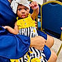 Na'Kyah is registered to the contest to win money with this photo: baby, child, headband, bow, yellow_top, striped_skirt, person, hand, indoor, chair, blue_clothing, skin, footwear, socks, curious_expression, seated, holding, portrait, infant, bright_colors
