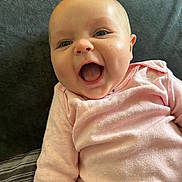 Margret Rellos is registered to the contest to win money with this photo: baby, infant, smiling, laughing, pink_clothing, cushion, blanket, indoor, face, happy, child, cute, person, portrait, head, skin, mouth_open, eyes, cheeks, sleepwear