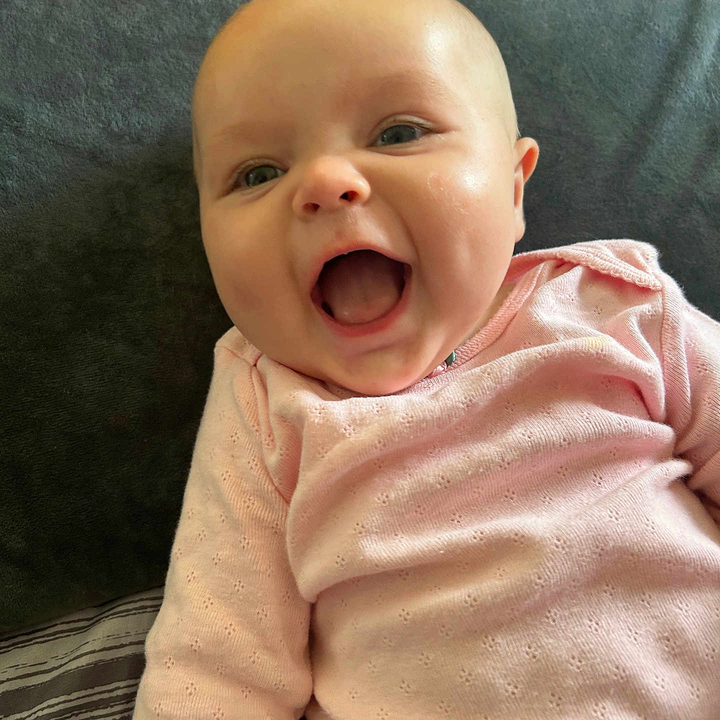 Margret Rellos is registered to the contest to win money with this photo: baby, blanket, cheeks, child, cushion, cute, eyes, face, happy, head, indoor, infant, laughing, mouth_open, person, pink_clothing, portrait, skin, sleepwear, smiling
