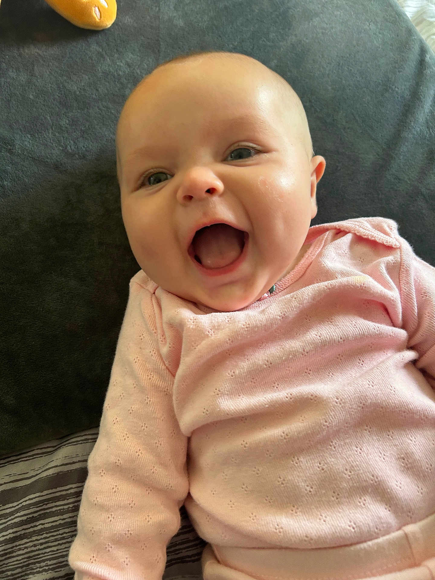Margret Rellos is registered to the contest to win money with this photo: baby, infant, smiling, laughing, pink_clothing, cushion, blanket, indoor, face, happy, child, cute, person, portrait, head, skin, mouth_open, eyes, cheeks, sleepwear