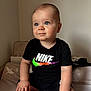 baby, background, black_clothing, blue_eyes, casual, child, cute, expression, face, furniture, hands, indoors, infant, nike_logo, person, portrait, short_hair, sitting, skin, soft_lighting