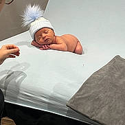 Frankie joined the competition — help win amazing prizes! newborn, baby, sleeping, hat, pom_pom, infant, person, glasses, hand, white_sheet, bed, indoor, portrait, cute, resting, soft, skin, child, tender, cozy