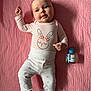 baby, infant, pink_blanket, pajamas, bunny_print, lying_down, bottle, cute, child, face, foot, hand, expression, soft_texture, indoors, portrait, sleepwear, small_object, relaxed, adorable