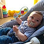 baby, pacifier, rattle, child, indoor, toy, chair, clothing, window, curtain, floor, plush_toys, colorful, infant, relaxing, person, cute, casual, home, seated