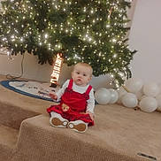 Willow joined the competition — help win amazing prizes! baby, child, christmas_tree, holiday, decorations, balloons, carpet, indoor, festive, lights, red_dress, white_shirt, floor, celebration, cute, sitting, infant, holiday_decor, home, portrait