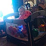 toddler, playpen, toys, indoor, child, pajamas, ball, stuffed_animal, window, furniture, room, floor, chair, cabinet, lighting, baby, person, play, soft_toys, backlight