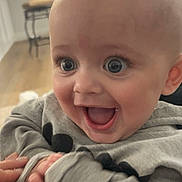 Reese joined the competition — help win amazing prizes! baby, infant, wide_eyes, surprised_expression, smile, open_mouth, tuft_of_hair, hoodie, hands, close_up, portrait, indoor, living_room, hardwood_floor, stool, cheek, eyelashes, cute, person, clothing