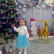 Melina a rejoint le concours — aidez-le/la à gagner de superbes lots ! blue_skirt, carpet, celebration, child, christmas_tree, decoration, festive, girl, golden_reindeer, holiday_decor, indoor, ornament, pigtails, present, smile, snowflakes, snowman, toy, white_top, winter