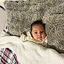 baby, blanket, fur_pillow, plaid, bed, infant, person, cozy, sleeping_area, soft_texture, clothing, cute, indoors, head, face, comfort, warm, resting, child, portrait