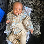 Kendryck is registered to the contest to win money with this photo: baby, beige_pants, blanket, casual, clothing, comfort, cozy, cushion, cute, face, indoor, infant, looking_at_camera, person, plaid_shirt, portrait, resting, soft_texture, striped_socks, young_child