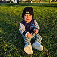 Gabriel a rejoint le concours — aidez-le/la à gagner de superbes lots ! beanie, blue_eyes, casual_clothing, child, daytime, grass, happy, hat, holding, houses, jacket, nature, outdoor, park, shoes, smiling, sunlight, toddler, trees, twig