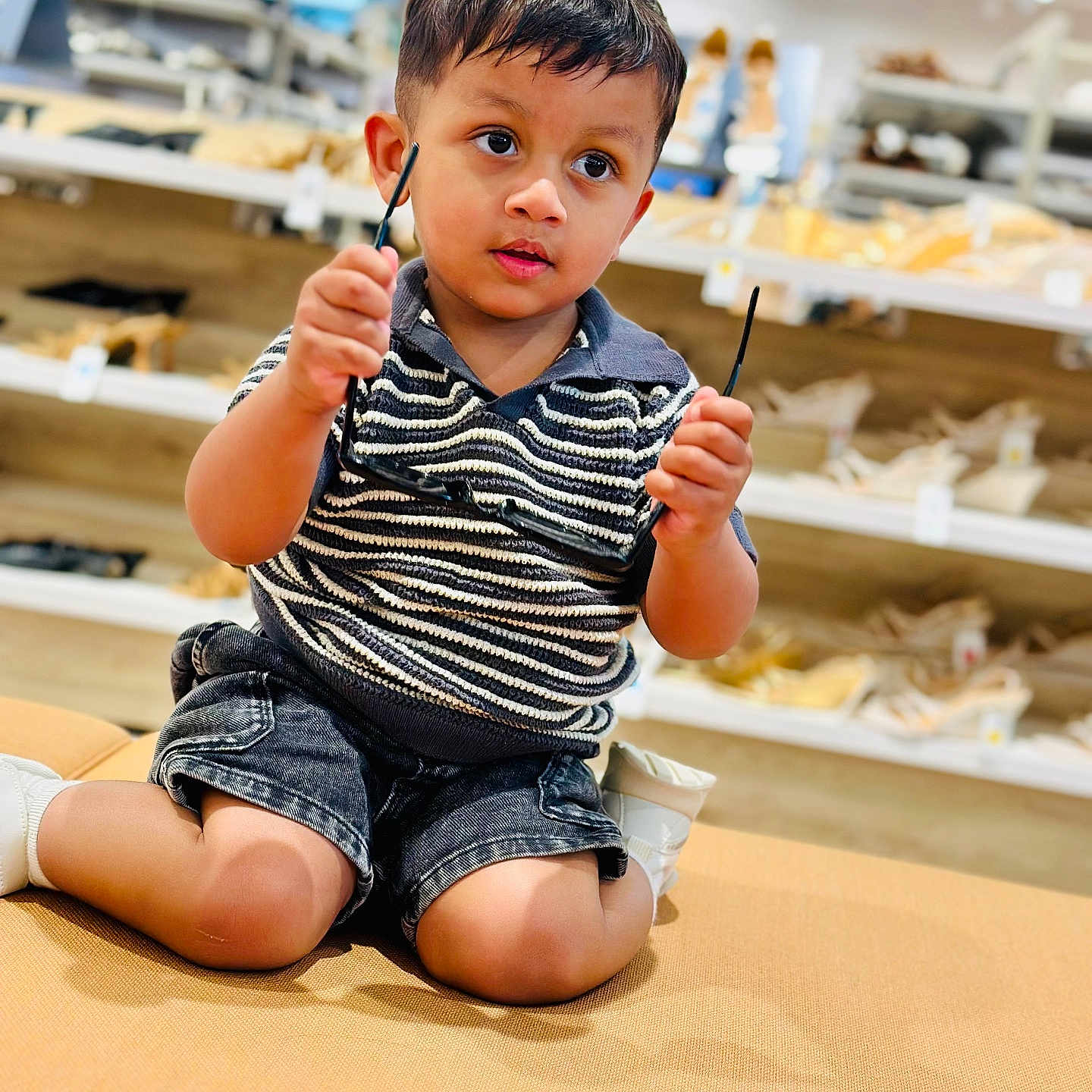 Jassman joined the competition — help win amazing prizes! bench, casual, child, clothing, curious, cushion, footwear, glasses, indoor, kneeling, person, portrait, shelves, shoes, shopping, shorts, store, striped_shirt, toddler, young_child