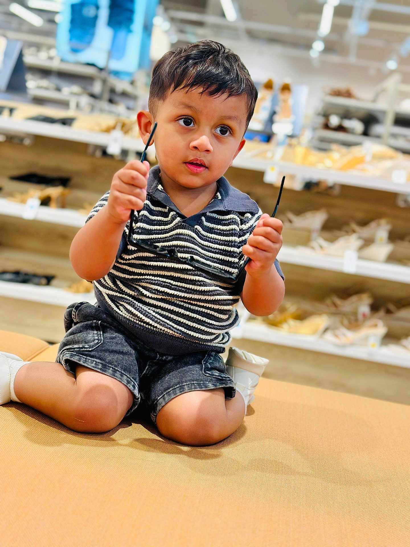 Jassman joined the competition — help win amazing prizes! toddler, child, glasses, kneeling, cushion, bench, store, shoes, shelves, clothing, shorts, striped_shirt, indoor, footwear, curious, young_child, person, portrait, casual, shopping