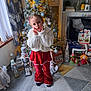 Gracie-Mae joined the competition — help win amazing prizes! child, christmas_tree, holiday_decorations, festive_clothing, red_outfit, white_jacket, indoor, floor_rug, toy_figures, nutcracker, fireplace, window, curtains, lights, smiling, posing, holiday_spirit, decorative_trees, present_boxes, home