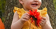 Patience is registered to the contest to win money with this photo: child, toddler, baby, smiling, portrait, outdoor, nature, tree, flower, red_flower, yellow_dress, sitting, happy, face, hands, garden, forest, daylight, colorful, photography