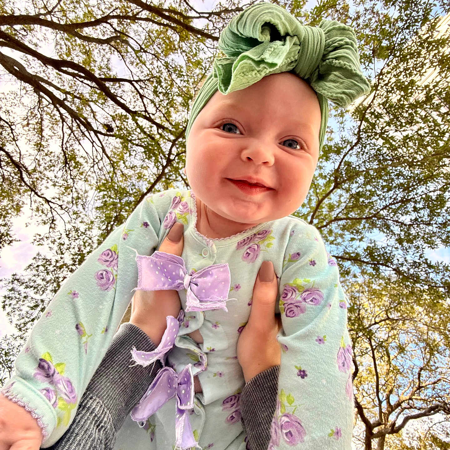 Davina is registered to the contest to win money with this photo: baby, child, smiling, headwrap, bow, onesie, floral_pattern, hands, trees, sky, outdoor, nature, person, portrait, happy, cute, infant, holding, fall, daylight