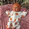 baby, infant, onesie, pumpkin_pattern, orange_hat, knitted_socks, jack_o_lantern, pink_blanket, soft_texture, cute, playful_expression, lying_down, indoors, newborn, clothing, face, hands, feet, smiling, child