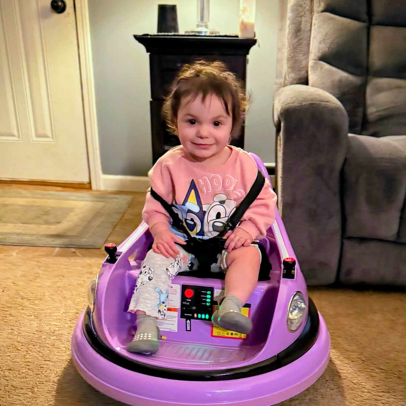 Caralyn joined the competition — help win amazing prizes! armchair, baby_bottle, carpet, child, cute, floor, furniture, hair, indoors, lamp, living_room, person, playtime, portrait, purple, seatbelt, smile, sweatshirt, toddler, toy_car