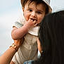 baby, child, hat, smiling, fingers_in_mouth, adult_hand, watch, denim_jacket, outdoor, sky, portrait, cute, happy, infant, person, holding, face, young_child, casual_clothing, daylight