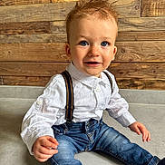 Jules participe au concours pour gagner de l'argent avec cette photo : toddler, child, boy, blue_eyes, white_shirt, suspenders, jeans, sitting, floor, wooden_wall, indoor, portrait, cute, smiling, happy, casual_clothing, young_child, fashion, hair, person