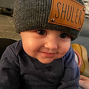 Shuler joined the competition — help win amazing prizes! baby, child, face, hat, knit_hat, sweater, smile, indoor, close_up, cute, infant, portrait, warm_lighting, cozy, expression, person, young_child, apparel, headwear, skin