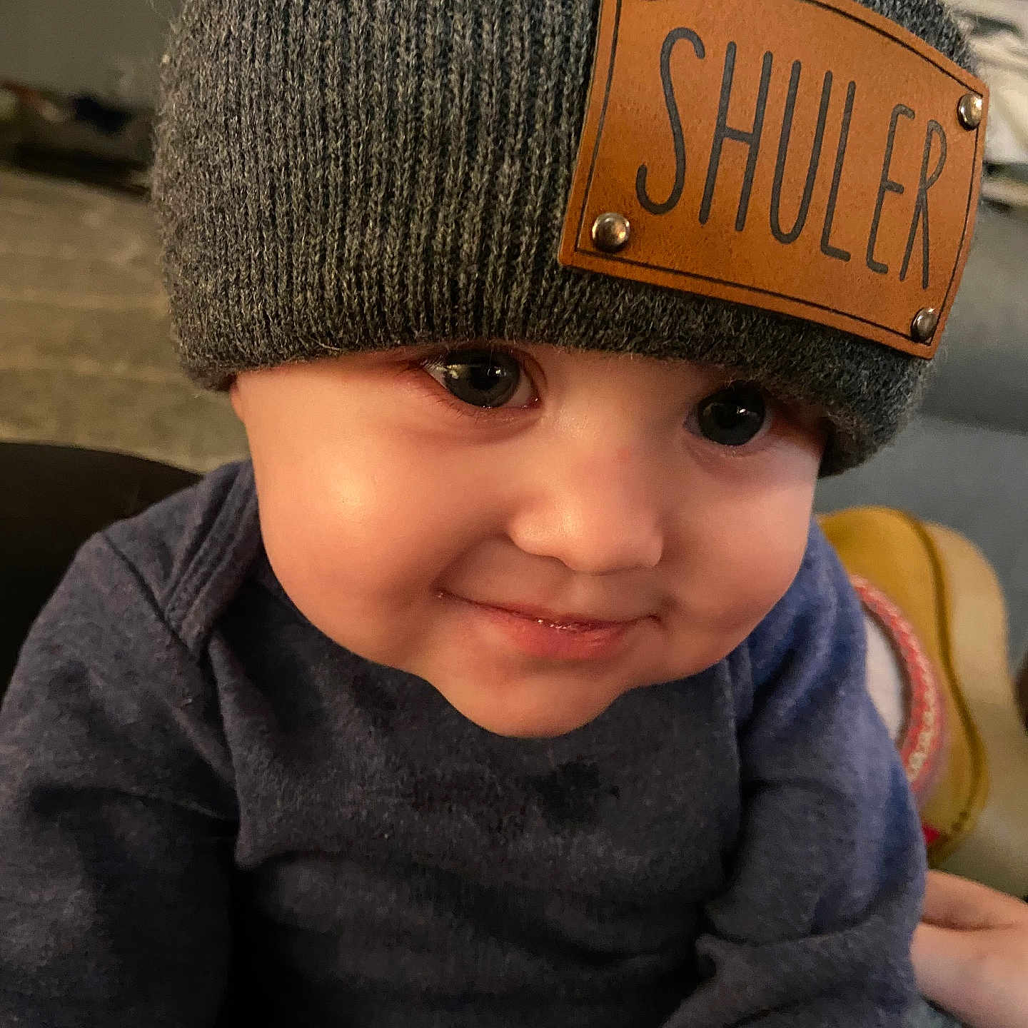 Shuler joined the competition — help win amazing prizes! apparel, baby, child, close_up, cozy, cute, expression, face, hat, headwear, indoor, infant, knit_hat, person, portrait, skin, smile, sweater, warm_lighting, young_child