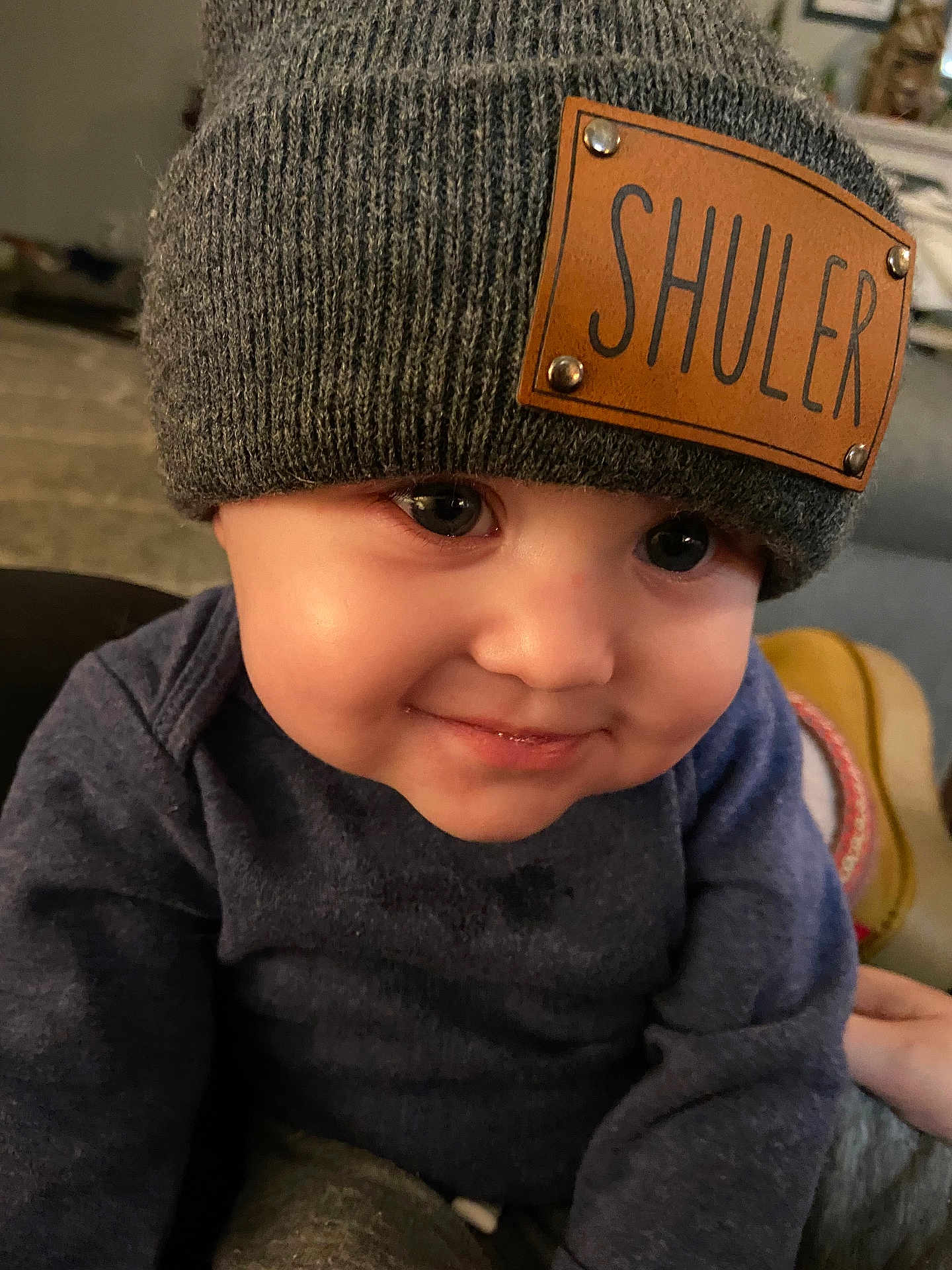 Shuler joined the competition — help win amazing prizes! baby, child, face, hat, knit_hat, sweater, smile, indoor, close_up, cute, infant, portrait, warm_lighting, cozy, expression, person, young_child, apparel, headwear, skin