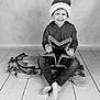 Brody is registered to the contest to win money with this photo: child, smiling, santa_hat, star, wooden_sled, barefoot, jeans, hoodie, floor, decoration, festive, holiday, black_and_white, portrait, indoor, happy, cute, sitting, toy, props