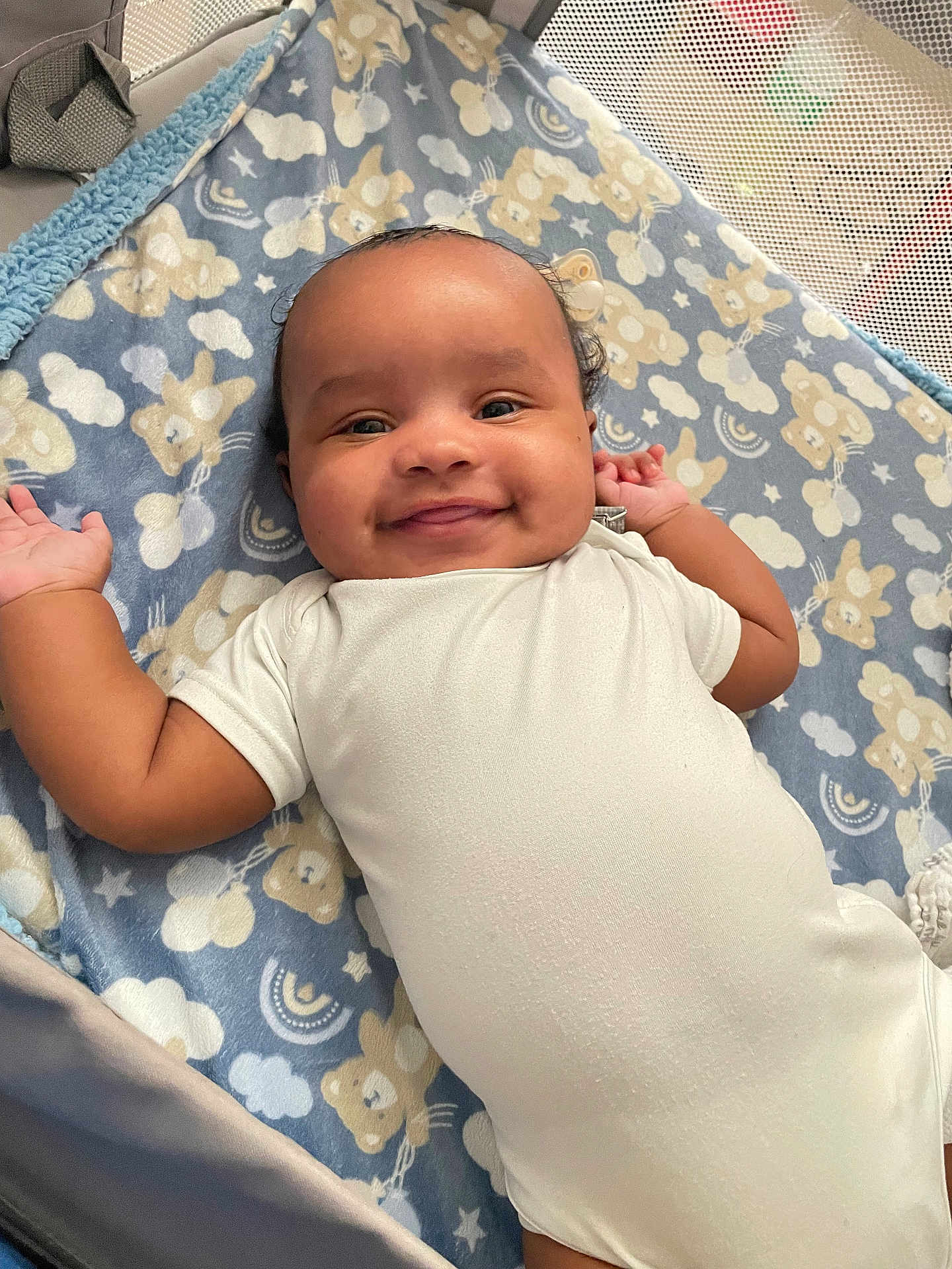 Kevin is registered to the contest to win money with this photo: baby, smiling, blanket, bear_pattern, cloud_pattern, onesie, playpen, infant, cute, happy, lying_down, child, soft_texture, indoors, portrait, face, head, arms, cozy, comfort