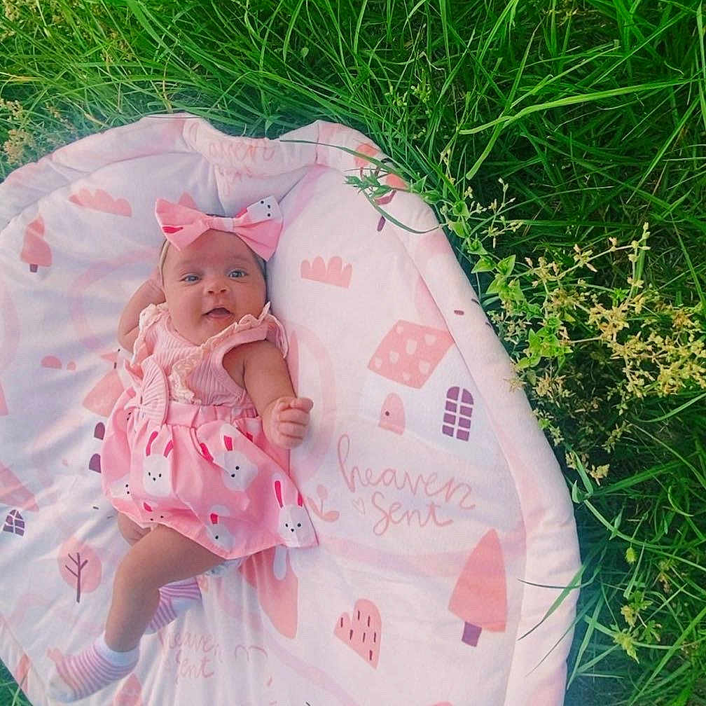 Rhyleee joined the competition — help win amazing prizes! baby, bow, child, cute, daytime, feet, grass, greenery, happy, headband, infant, legs, lying_down, nature, outdoor, pink_dress, playmat, smiling, soft_toys_pattern, sunlight