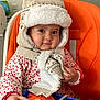 baby, cheeks, child, colorful, curious, cute, face, hand, hat, indoor, infant, knitted, orange_high_chair, person, play, scarf, seated, smile, toy, warm_clothing