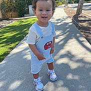 Karter joined the competition — help win amazing prizes! toddler, child, smiling, outdoor, sidewalk, sunlight, shadows, trees, greenery, grass, overalls, cartoon_patch, sneakers, white_shoes, curly_hair, happy, person, walking, daylight, nature