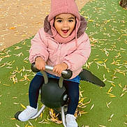 Sana a rejoint le concours — aidez-le/la à gagner de superbes lots ! toddler, child, pink_jacket, pom_pom_hat, spring_rider, playground, leaves, outdoor, smiling, happy, fall, fence, sign, green_ground, white_shoes, denim_skirt, play, person, toy, cold_weather