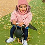 toddler, child, pink_jacket, pom_pom_hat, spring_rider, playground, leaves, outdoor, smiling, happy, fall, fence, sign, green_ground, white_shoes, denim_skirt, play, person, toy, cold_weather