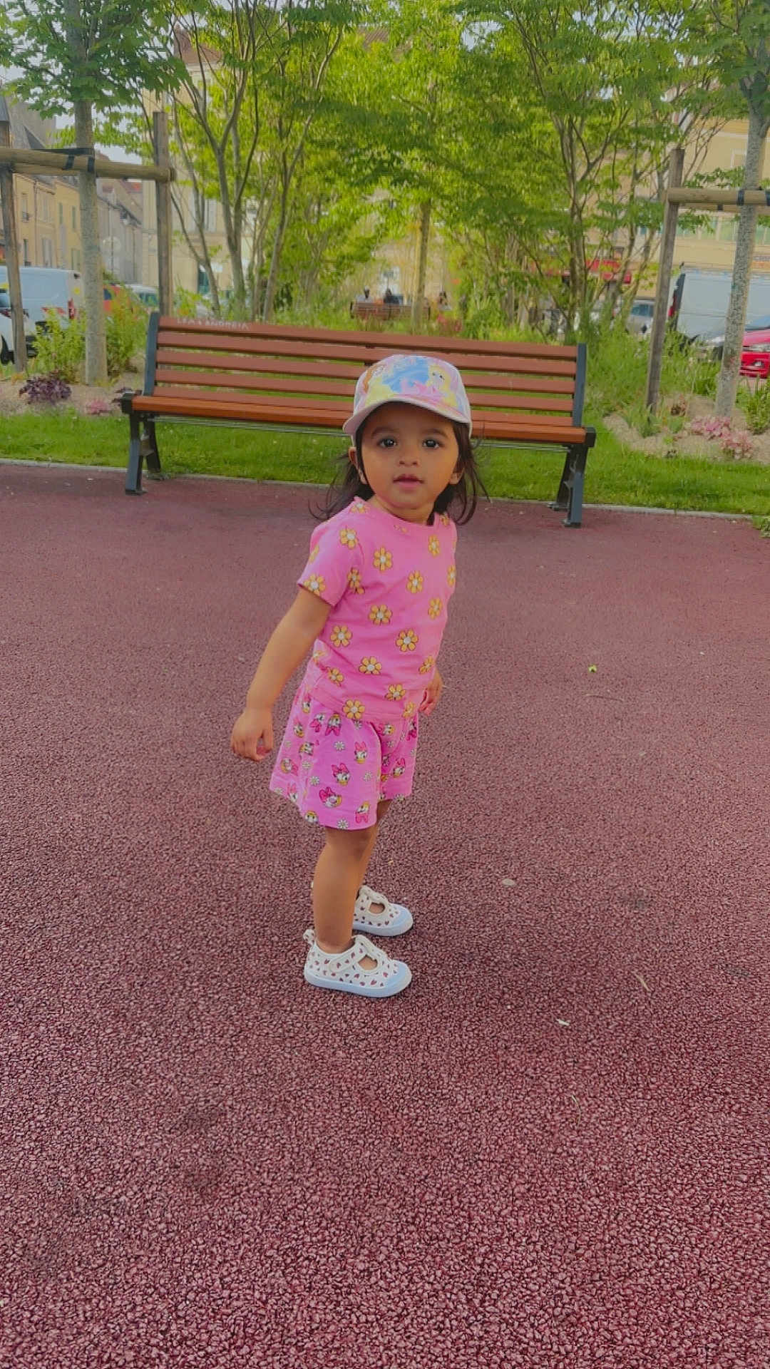 Sana participe au concours pour gagner de l'argent avec cette photo : child, toddler, pink_clothing, hat, cap, outdoor, playground, bench, trees, greenery, shoes, curious, standing, daylight, park, nature, young_child, casual_wear, person, summer