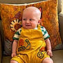 baby, bald_head, casual, child, colorful_clothing, comfortable, couch, cute, decorative_pillow, happy, home, indoor, infant, patterned_pillow, portrait, seated, smiling, soft_lighting, striped_shirt, yellow_overalls