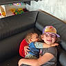 child, children, hug, couch, glasses, cap, toy, shelf, happy, smile, indoor, leather, clothing, playful, family, affection, cozy, young, toddler, sitting