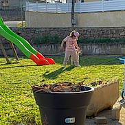 Lola participe au concours pour gagner de l'argent avec cette photo : child, grass, slide, playground, outdoor, sunlight, shadow, cap, pink_clothing, house, fence, flower_pot, garden, concrete, daytime, person, toy, nature, recreation, leisure