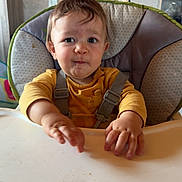 Elio participe au concours pour gagner de l'argent avec cette photo : toddler, child, high_chair, yellow_shirt, expression, indoor, kitchen, baby, face, hands, seatbelt, table, food_crumbs, curious, person, furniture, home, portrait, young_child, messy
