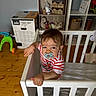 Elio participe au concours pour gagner de l'argent avec cette photo : toddler, crib, pacifier, child, toy, shelf, stuffed_animal, wooden_floor, indoor, baby, furniture, clothing, person, room, home, playroom, smiling, holding, striped_shirt, curious