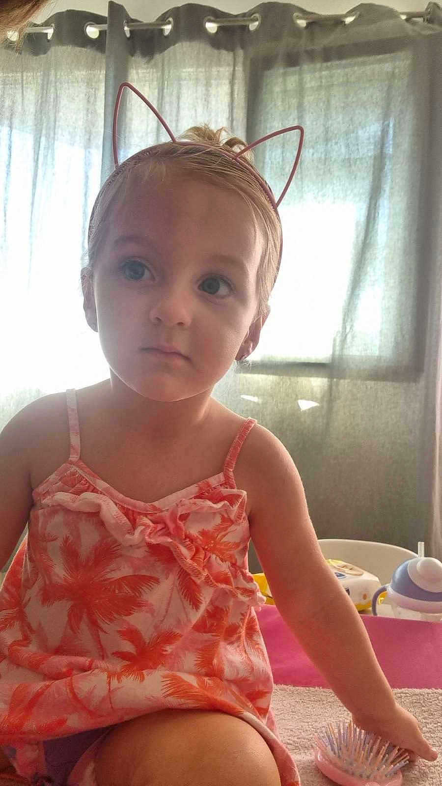 Celia a rejoint le concours — aidez-le/la à gagner de superbes lots ! toddler, child, girl, indoor, curtains, cat_ear_headband, dress, hairbrush, sippy_cup, toy, window, furniture, pink, orange, person, young_child, expression, sitting, casual, portrait