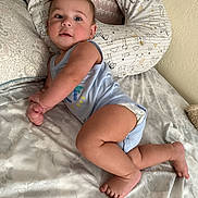 Noah is registered to the contest to win money with this photo: baby, infant, bed, pillow, onesie, diaper, skin, foot, hand, face, eyes, smile, curly_hair, fabric, pattern, indoor, cute, child, lying_down, cozy