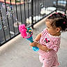 Ailany Hernández joined the competition — help win amazing prizes! balcony, barefoot, bracelet, bubble, child, concrete_floor, cute, daylight, dinosaur, hair_ties, happy, outdoor, pink, playful, railing, side_profile, striped_clothing, summer, toddler, toy