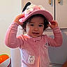 Ailany Hernández joined the competition — help win amazing prizes! cabinet, cap, casual, child, colorful, curly_hair, cute, expression, face, furniture, hat, home, indoor, person, pink_clothing, playful, standing, toddler, toy, young_child