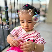 Ailany Hernández is registered to the contest to win money with this photo: balcony, bracelet, bubbles, child, colorful, curious, cute, daylight, focus, outdoor, person, pigtails, play, portrait, railing, small_hands, striped_shirt, toddler, toy, young_child
