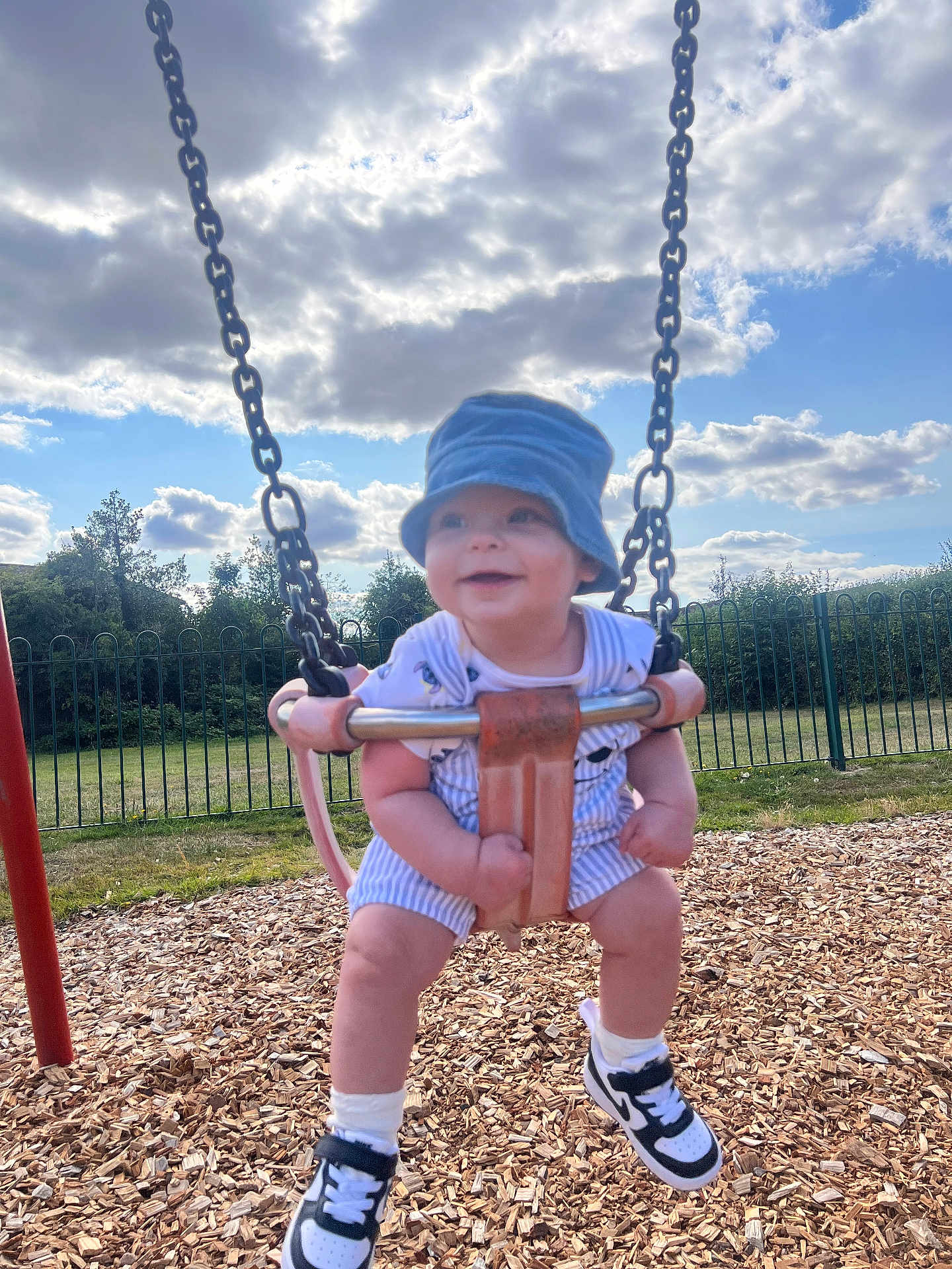 Tommy joined the competition — help win amazing prizes! toddler, child, swing, playground, hat, smiling, outdoor, daylight, wood_chips, fence, grass, clouds, blue_sky, shoes, socks, romper, happy, person, summer, fun