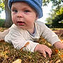 Tommy is registered to the contest to win money with this photo: baby, child, blue_hat, autumn_leaves, grass, outdoor, nature, tree_trunk, crawling, closeup, face, skin, hand, young_child, fall, daylight, person, casual_clothing, headwear, park