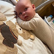 Tommy is registered to the contest to win money with this photo: baby, infant, blanket, teddy_bear, onesie, carpet, baby_products, toy, floor, indoor, child, person, cute, sleeping_area, soft_texture, pillow, gaze, head, skin, clothing