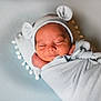 newborn, baby, sleeping, swaddled, blanket, hat, bear_ears, cushion, pom_pom, soft_texture, peaceful, infant, portrait, indoors, cute, resting, child, wrapped, cozy, head